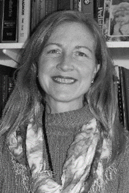 In this black and white picture, Marilyn is pictured as a white woman with long hair. She is wearing a light-colored scarf and a sweater. Behind her is a bookcase. 